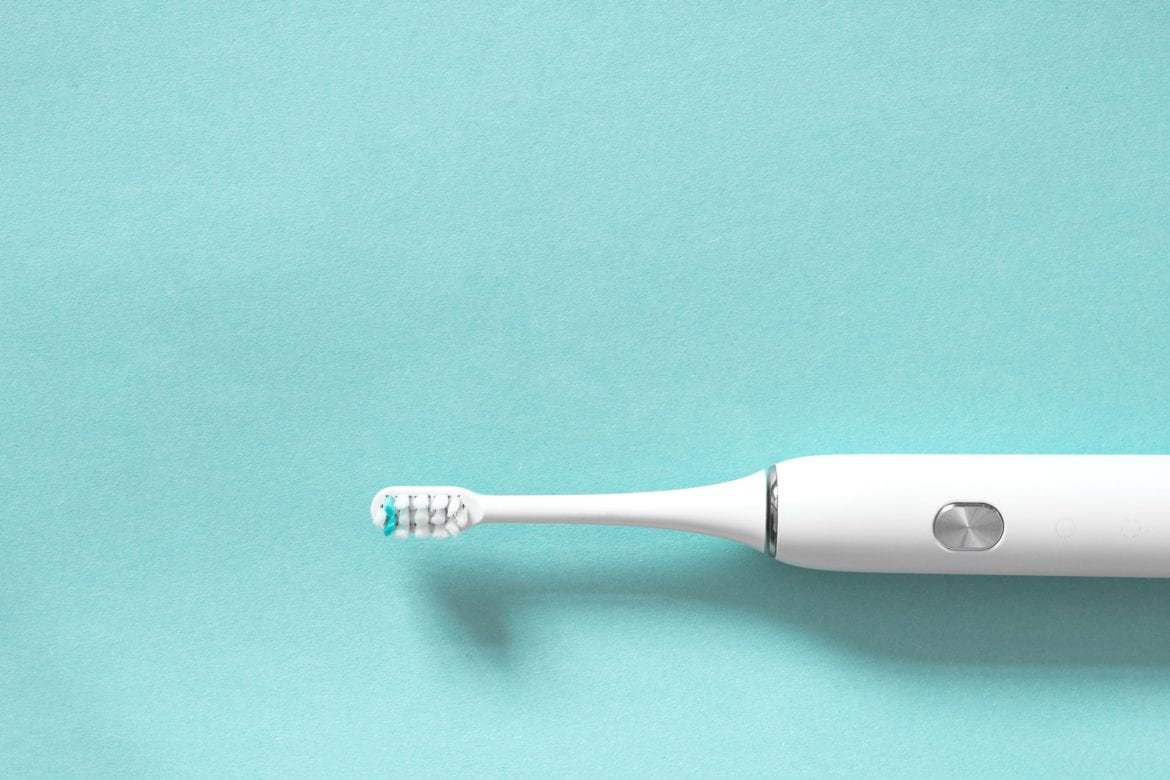 An electric tooth brush sitting on a light teal surface