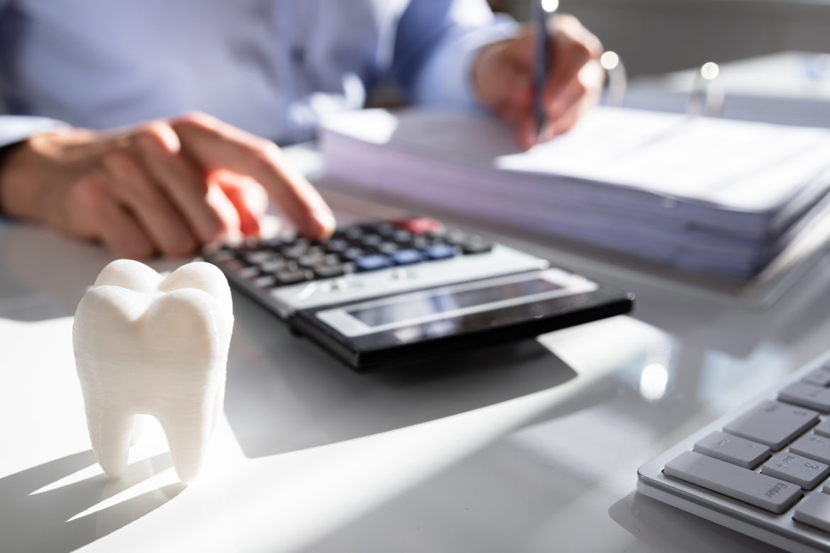person using a calculator next to a white tooth model