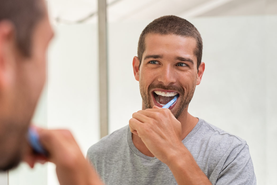 A man is smiling while brushing his teeth.