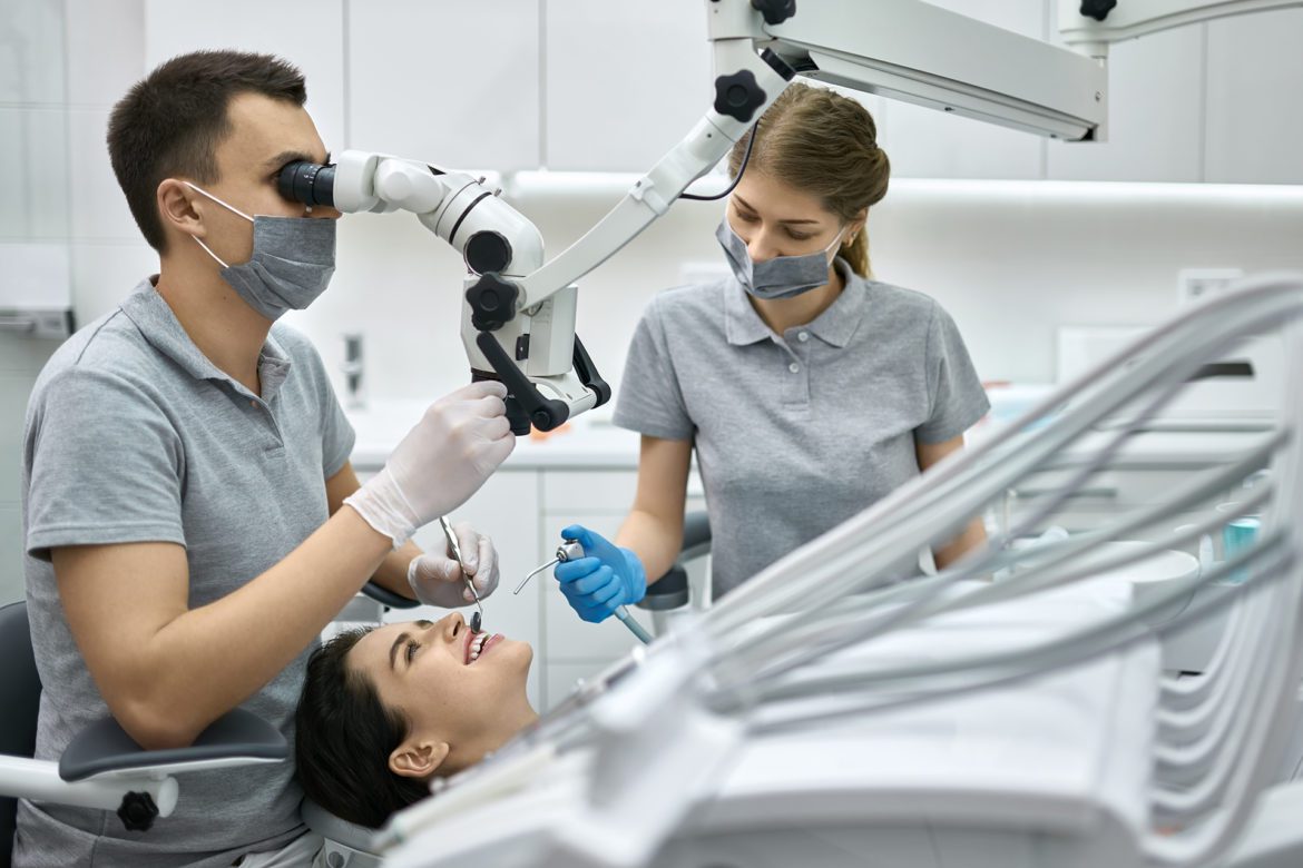 Deintist and assistant looking at a patient's teeth through a microscope