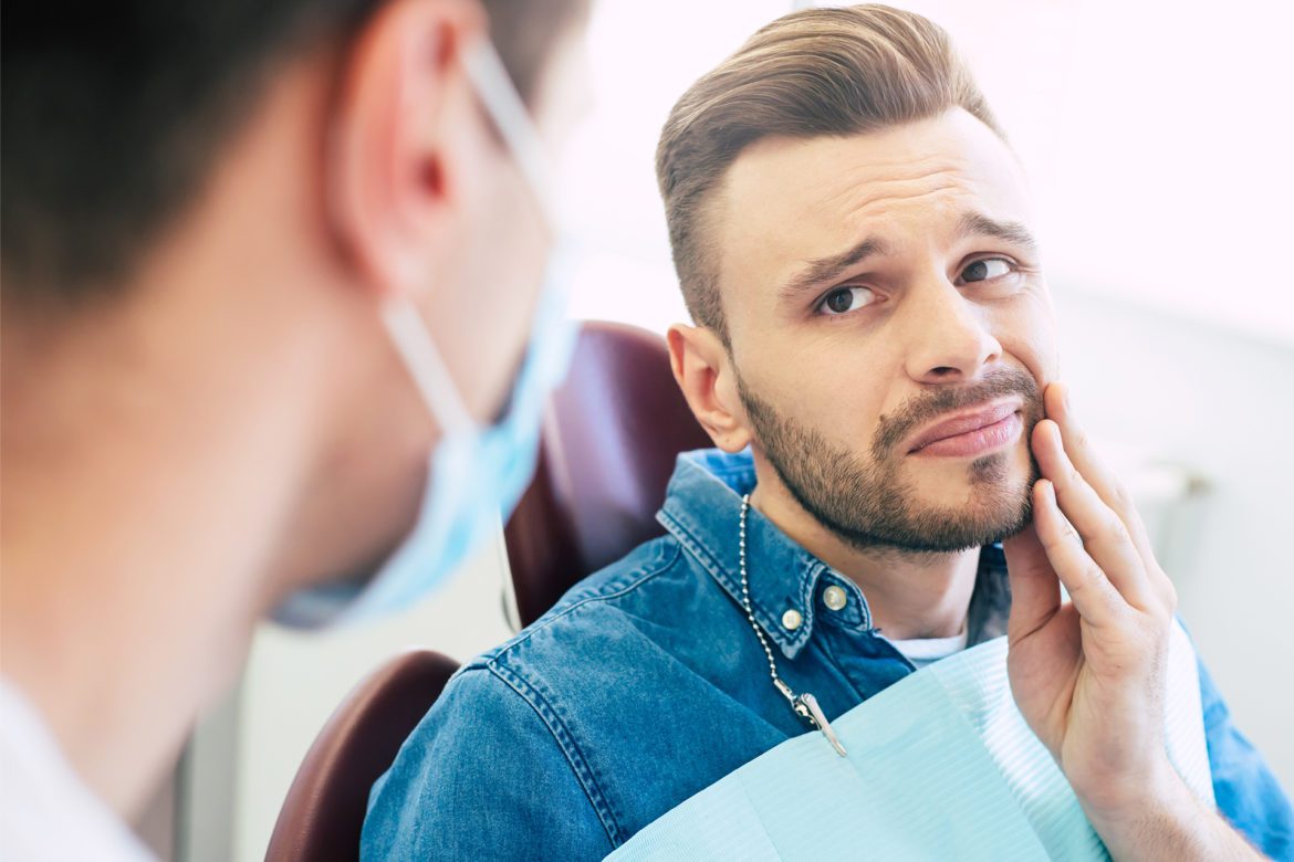 A man is holding the side of his jaw while talking with a dentist.
