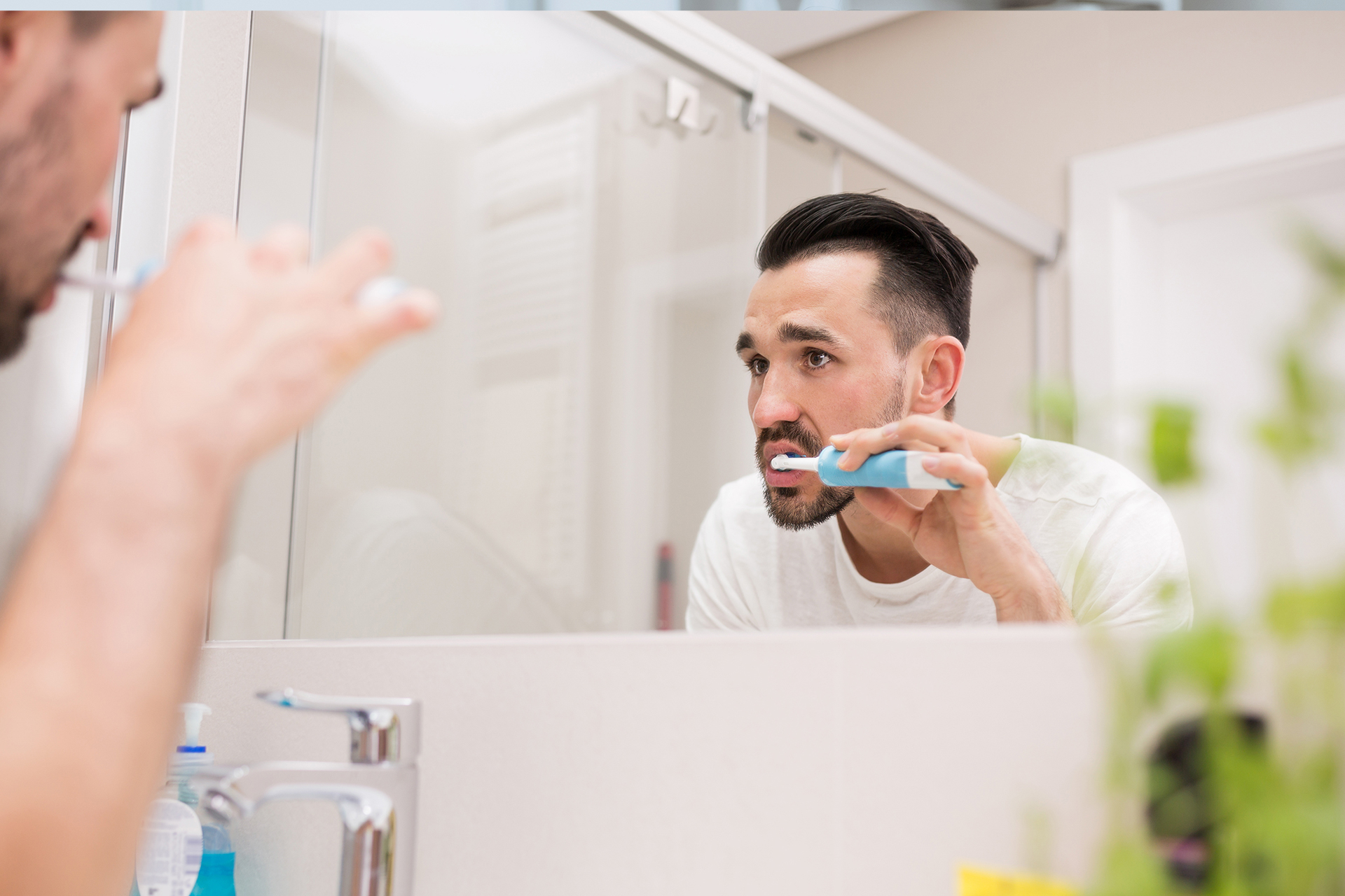 man brushing teeth while looking in the mirror