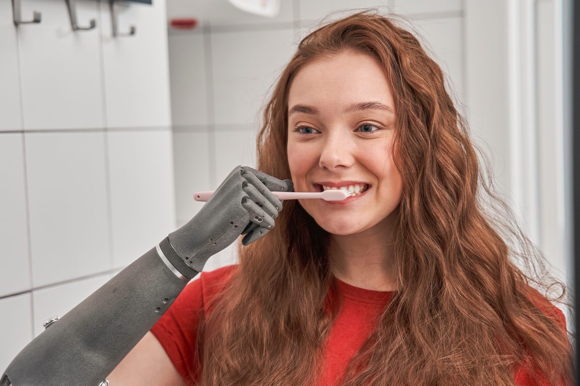 blog-eds-dentdisability A woman with an artificial arm is brushing her teeth.