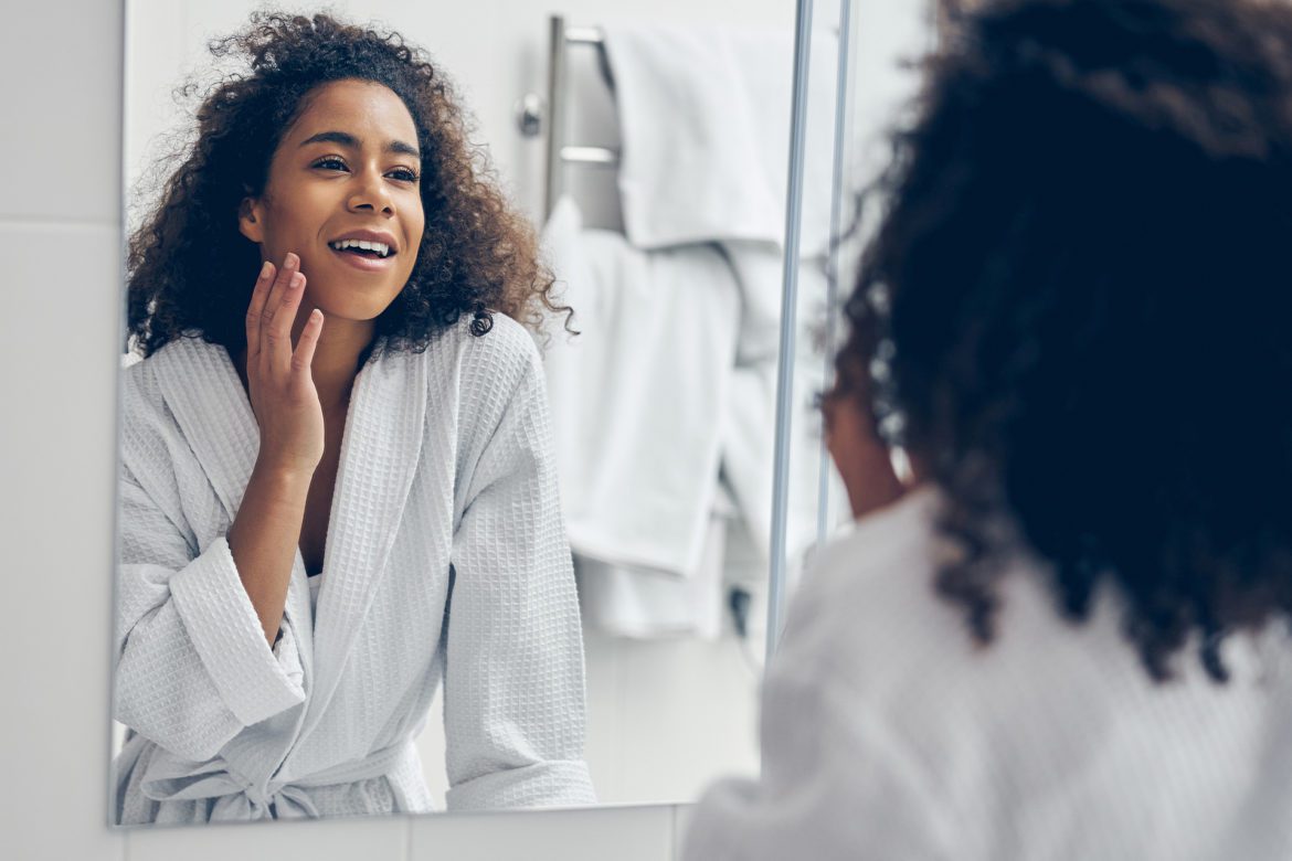 Woman looking in the mirror while touching the side of her mouth.