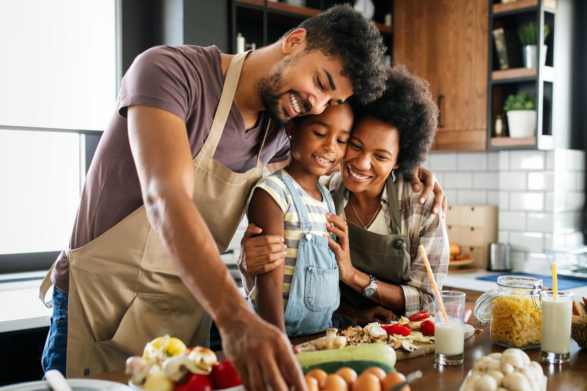 A family of three prepares food in the kitchen.
