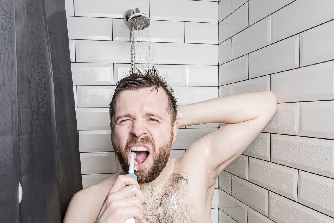 A man is brushing his teeth in the shower.