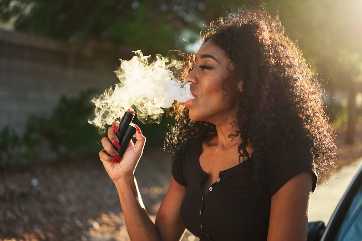 Woman using vaping pen and blowing out smoke