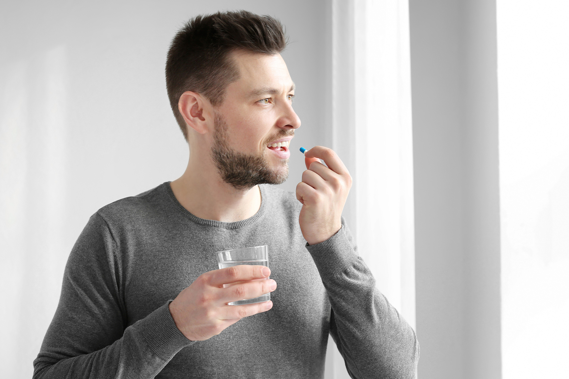 eds - Male taking pill with glass of water in hand.